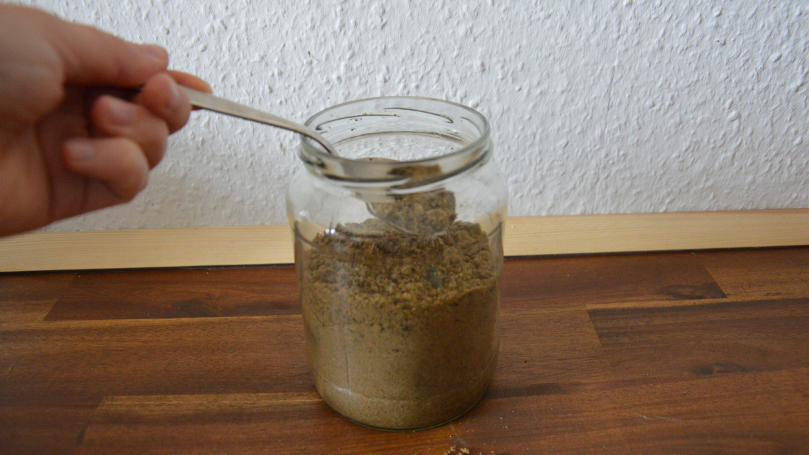 Glas mit Erde mit Hilfe eines Löffels befüllen