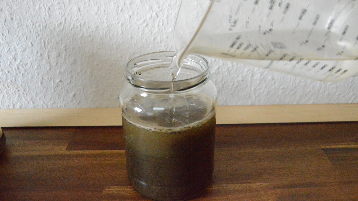 Mit Erde befülltes Glas mit Wasser auffüllen